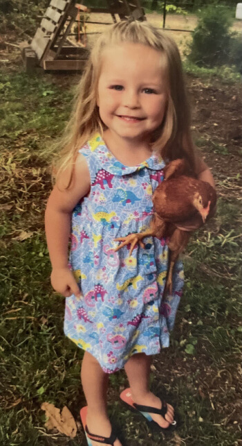 Children and chickens – a perfect match! A little blonde girl in a summer dress holds her chicken.