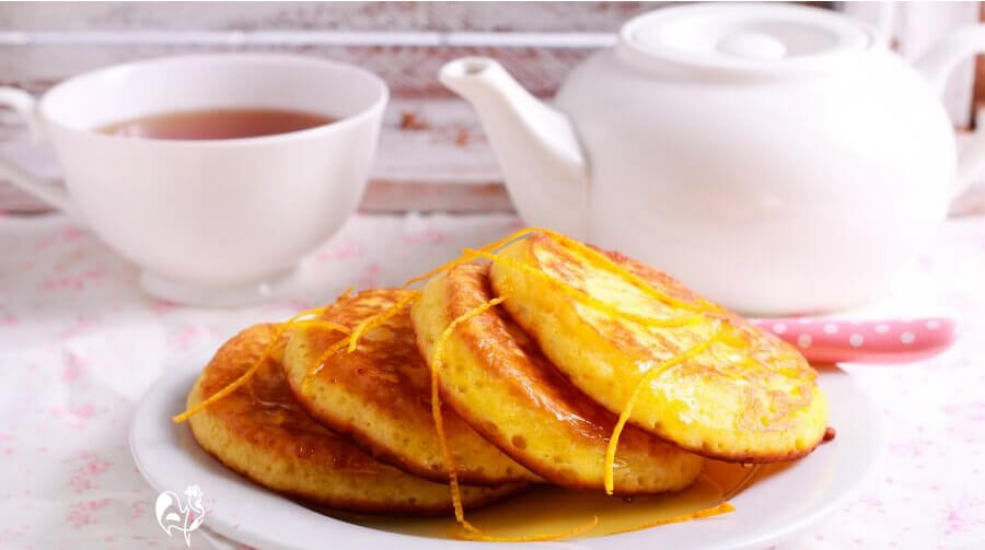 Two Scotch pancakes with butter and jam and a pot of tea.